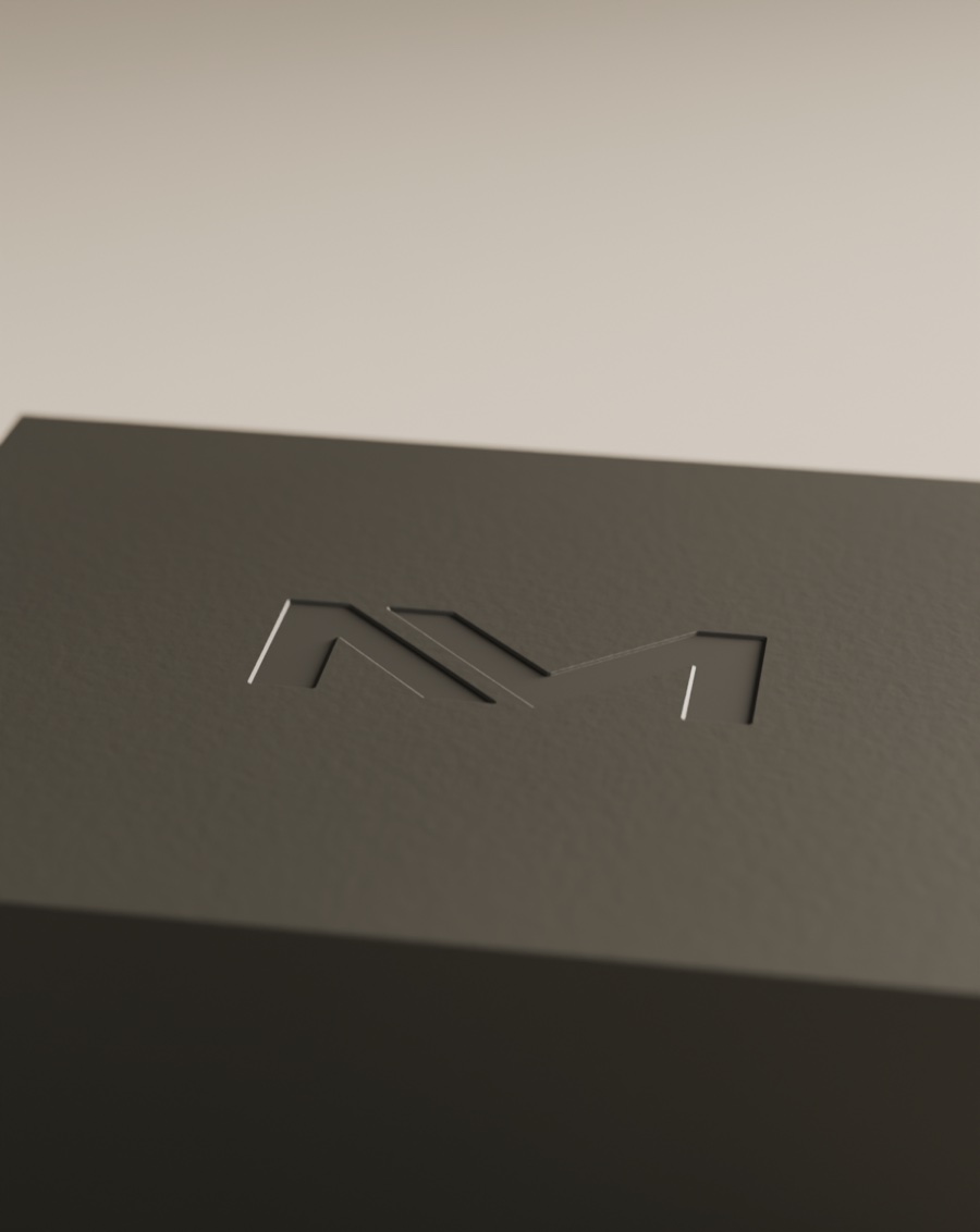 Monograma Niven Mark hundido en bajorrelieve sobre la tapa de un estuche de polímero mate carbón, revelado por una luz rasante.